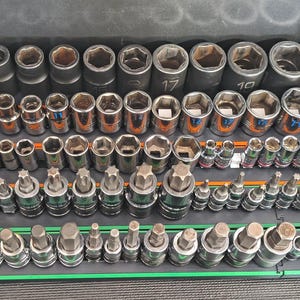 May include: A collection of metal socket wrench attachments and driver bits organized in rows on colored plastic trays. The set includes various sizes of hexagonal and star-shaped sockets with numerical markings, arranged neatly inside a dark tool drawer.