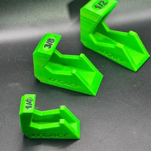 May include: Three bright green 3D-printed leveling shims with the text "LEGACY" and fractional measurements of 1/4, 3/8, and 1/2. The shims are angled and designed to provide support or adjustment.