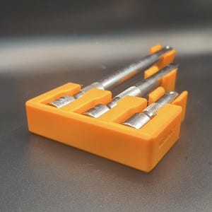 May include: An orange tool holder with three metal tools. The holder is rectangular with slots to hold the tools upright. The tools have silver handles and different shaped heads.