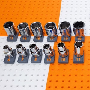 May include: A set of chrome sockets of various sizes, arranged on a gray base. The sockets are labeled with numbers ranging from 6 to 19. The background is a white and orange pegboard.