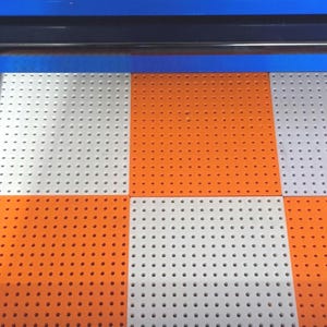 May include: A set of square pegboard panels arranged in a checkerboard pattern of alternating light gray and bright orange colors. Each panel features a uniform grid of small, circular holes throughout the surface, set inside a blue metal frame.