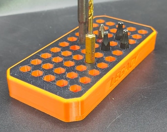 May include: A rectangular orange storage tray with a black top insert featuring a grid of hexagonal holes. The tray has the word LEGACY embossed on the side. Several metal drill bits and tool accessories are inserted into the hexagonal slots.