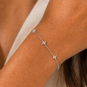 May include: A delicate silver-toned chain bracelet featuring evenly spaced floral-shaped charms. Each charm is composed of four small, clear, round-cut stones arranged in a petal pattern, connected by a thin, polished metal link chain.