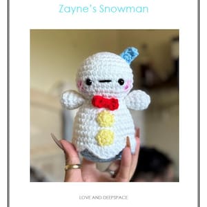 May include: A crocheted snowman with a blue hat, red bow tie, and yellow buttons. The snowman has black eyes and pink cheeks. Text on the image reads "Zayne's Snowman" and "LOVE AND DEEPSPACE".