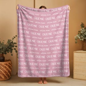 Puede incluir: Una manta suave de color rosa empolvado con un patr&oacute;n repetitivo del nombre Chloe Mae impreso en blanco. El texto alterna entre una fuente sans-serif en negrita en may&uacute;sculas y una delicada fuente cursiva en min&uacute;sculas por toda la tela.