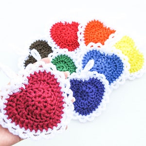 May include: A collection of colorful, crocheted heart-shaped items. Each heart is a different color, including red, orange, yellow, green, blue, and brown, with a white, scalloped border. One heart is held in a hand.