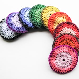 May include: A collection of handmade, crocheted coasters in a rainbow of colors. Each coaster is circular, with a gradient effect from the center to the outer edge. Colors include purple, blue, green, yellow, orange, and red. The coasters are arranged in a curved line.