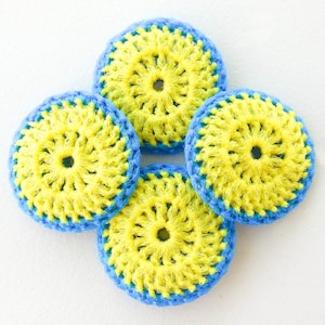 May include: Four handmade crochet coasters. Each coaster features a bright yellow center with a blue border. The coasters are arranged in a symmetrical pattern, showcasing the vibrant color combination and intricate stitch work.