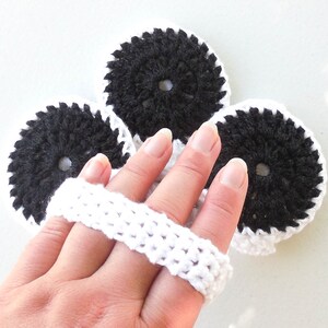 May include: Crocheted black and white coasters. The coasters are circular with a black center and a white border. A white crocheted finger strap is visible.