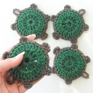 Op de afbeelding: Vier handgemaakte gehaakte schildpad applicaties. Elke schildpad heeft een groen midden en een bruine rand, met kleine, gedetailleerde poten en kop. De schildpadden zijn gerangschikt in een vierkant patroon.