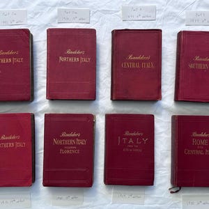 Könnte beinhalten: Acht alte Baedeker-Reiseführer mit roten Stoffeinbänden und goldener Prägung. Die Titel umfassen Northern Italy, Central Italy, Southern Italy sowie Rome and Central Italy. Jedes Buch ist mit einem kleinen weißen Papieretikett versehen.