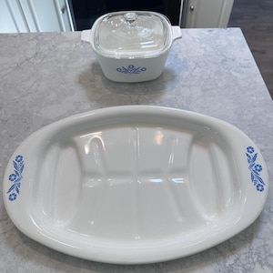Könnte beinhalten: Weißes ovales Serviertablett und quadratische Auflaufform mit blauen Blumenmustern. Das Tablett hat drei geteilte Abschnitte und Griffe. Die Auflaufform hat einen Glasdeckel. Beide stehen auf einer grauen Arbeitsplatte.