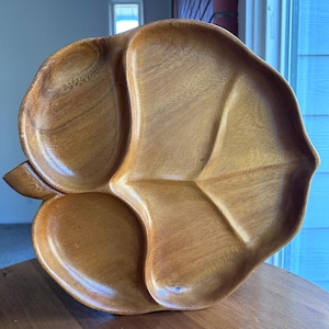 Puede incluir: Una bandeja de madera con forma de hoja con múltiples compartimentos. La bandeja está hecha de madera de color marrón claro y tiene un patrón de vetas de madera natural. La bandeja está diseñada para parecerse a una hoja con un tallo y venas.