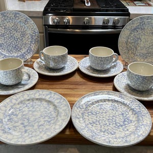 May include: A set of four ceramic cups and saucers with four matching plates, all featuring a light blue and white speckled sponge-painted pattern. The cups have a cream-colored interior, while the plates and saucers have a consistent mottled finish.