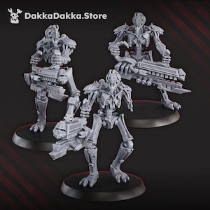 May include: Three gray robotic figures, each posed on a black circular base, are displayed. The figures have detailed mechanical designs, holding large, futuristic weapons. The text "DakkaDakka.Store" is visible in the upper left corner.