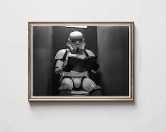 Op de afbeelding: Zwart-wit ingelijste print met een Stormtrooper uit Star Wars die een boek leest. De Stormtrooper draagt een volledig harnas, zit en houdt het open boek vast. Een humoristische afbeelding.