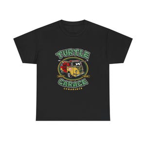 Puede incluir: Camiseta negra con un gráfico colorido de una furgoneta vintage. El diseño incluye las palabras "Turtle Garage" y "Cowabunga". La furgoneta es roja y amarilla con una tabla de surf encima. El diseño incluye las palabras "Service" y "Repair".