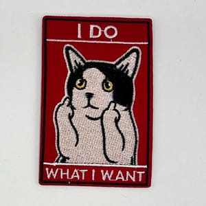 May include: Embroidered patch with a red background and a black border. The patch features a cat with black and white markings, yellow eyes, and raised middle fingers. The text "I DO" is at the top, and "WHAT I WANT" is at the bottom.