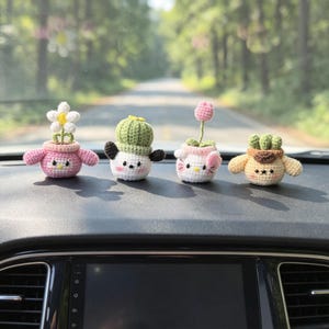 May include: Four small, crocheted figures shaped like potted plants and animals. The figures feature pastel colours, including pink, white, green, and tan, with embroidered facial details. Each piece is crafted with yarn and has a rounded, plush appearance.