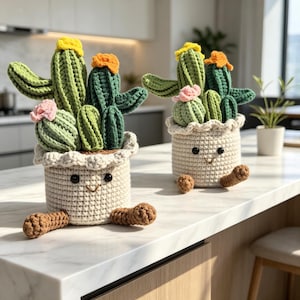May include: Two crocheted cactus plants in cream-colored pots with embroidered faces, brown feet, and ruffled rims. Each cactus features shades of green yarn, topped with small yellow, orange, and pink crocheted flowers, creating a soft texture.