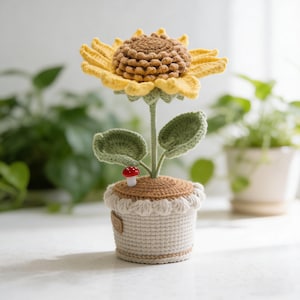 May include: A crocheted sunflower in a pot. The sunflower has yellow petals and a brown center. The green leaves and stem support the flower. The pot is beige with a brown rim and a small red and white mushroom. The pot is decorated with a beige trim.