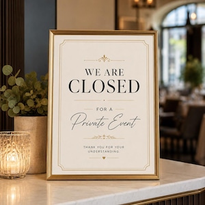 May include: A gold-framed sign with a cream background and black text that reads: WE ARE CLOSED FOR A PRIVATE EVENT. THANK YOU FOR YOUR UNDERSTANDING. The sign features decorative gold lines and small flourishes, centred on a white surface.