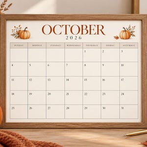 May include: A framed wall calendar for October 2026 with a wood-toned frame. The calendar features a white background with brown text, a grid layout for the days of the month, and illustrations of orange pumpkins with autumn leaves on both sides.