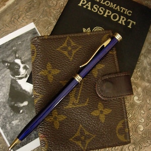 May include: A brown leather wallet with a gold pen and a black passport that says "Diplomatic Passport".