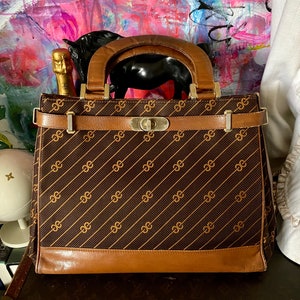 May include: A brown leather handbag with a gold chain and a brown and gold patterned fabric body. The bag has a top handle and a buckle closure.