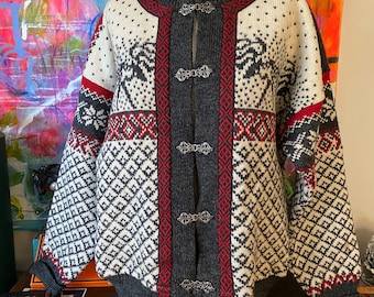 May include: A white, gray, and red patterned cardigan sweater with a round neckline and silver clasps. The sweater features a geometric and snowflake design. The sweater is displayed on a mannequin with a pearl necklace.
