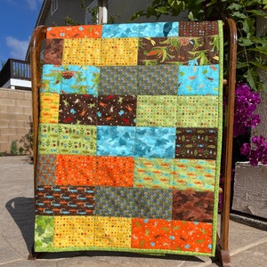 May include: A patchwork quilt with a variety of colorful fabrics featuring different patterns, including camouflage, polka dots, and geometric designs. The quilt is displayed on a wooden rack.