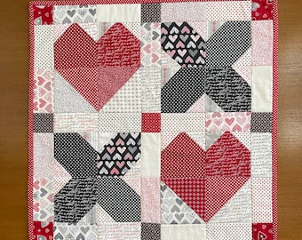 May include: A red, white, and black patchwork quilt with a heart design. The quilt is made of various fabrics with different patterns, including polka dots, hearts, and script.