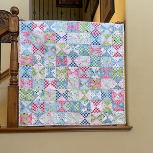 May include: A patchwork quilt with a variety of floral and geometric patterns in shades of pink, blue, green, and white. The quilt is made up of small squares and triangles, and it has a white border.