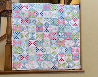 May include: A patchwork quilt with a variety of floral and geometric patterns in shades of pink, blue, green, and white. The quilt is made up of small squares and triangles, and it has a white border.