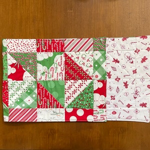 May include: A quilted Christmas-themed table runner. The patchwork design features red, green, and white fabrics with patterns of candy canes, snowmen, and polka dots. The runner is rectangular and appears to be handmade.
