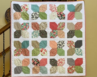 May include: A patchwork quilt with a white background and a variety of floral and geometric patterns in shades of pink, green, and black.