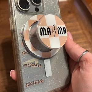 May include: A clear glitter phone case with a pop-up grip. The grip has a peach and white checkered pattern with the word "mama" in black with a lightning bolt. The phone case has leopard print accents.