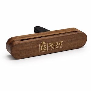 May include: A rectangular, wooden car air freshener with rounded edges. The air freshener has a black clip and the text "GELUXE SCENTS" in gold. The logo "GS" is also in gold.