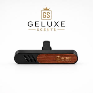Könnte beinhalten: Schwarzer Auto-Lufterfrischer mit Holzmaserungsakzent und dem Text "GELUXE SCENTS". Der Lufterfrischer hat einen Clip zur Befestigung und ein Logo mit den Buchstaben "GS" und einer Krone.