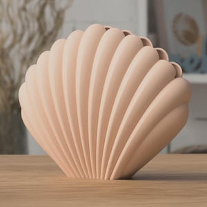 Könnte beinhalten: Eine blass pfirsichfarbene Vase in Form einer fächerartigen Muschel. Das Objekt weist eine Reihe vertikaler, abgerundeter Rippen auf, die von der Basis bis zum oberen Rand verlaufen und eine symmetrische, gewellte Silhouette mit matter Oberfläche bilden.