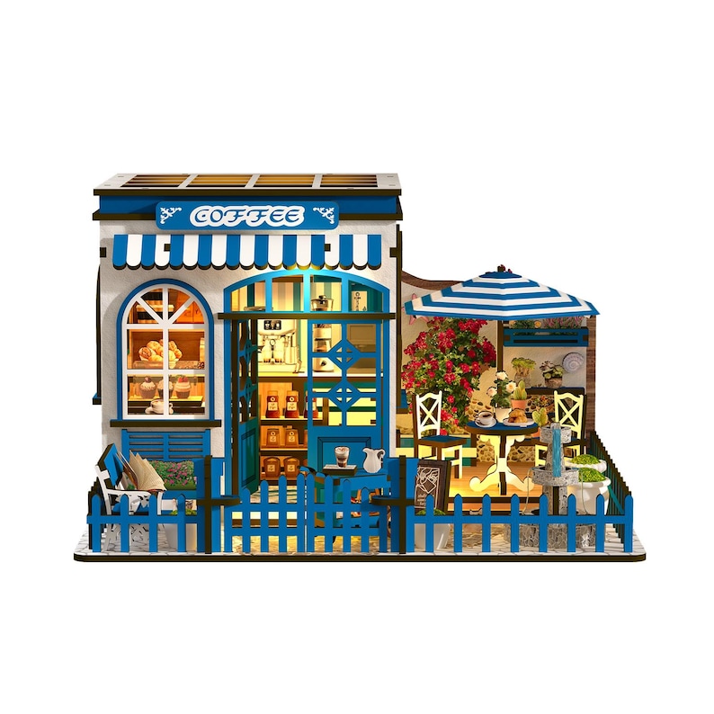 May include: Miniature coffee shop model with blue and white accents. Features a striped awning, a small outdoor seating area with a striped umbrella, and a decorative fence. The shop has a sign that says "Coffee".