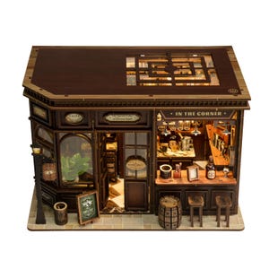 May include: A detailed wooden model of a wine shop, featuring a bar, stools, and a barrel. The sign reads "IN THE CORNER". The shop has a dark brown exterior and a lit interior. The model includes the text "Wine Shop".