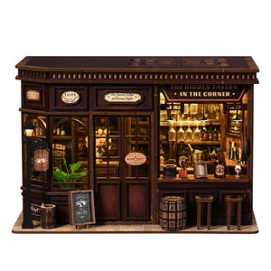 May include: A detailed miniature wooden tavern model. The facade includes signs reading "TASTY" and "The Hidden Tavern - In The Corner." The interior is lit, revealing bottles, glasses, and a bar. A small chalkboard displays "SIMPLE TEXT".