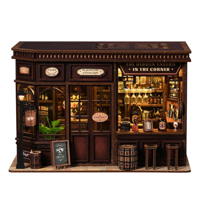 May include: A detailed miniature wooden tavern model. The facade includes signs reading "TASTY" and "The Hidden Tavern - In The Corner." The interior is lit, revealing bottles, glasses, and a bar. A small chalkboard displays "SIMPLE TEXT".