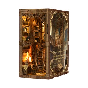 May include: A wooden bookshelf model with intricate details, featuring a staircase, bookshelves, and warm lighting. The model has a quote on the side that reads, "A free man obtains knowledge From many sources I besides Books."
