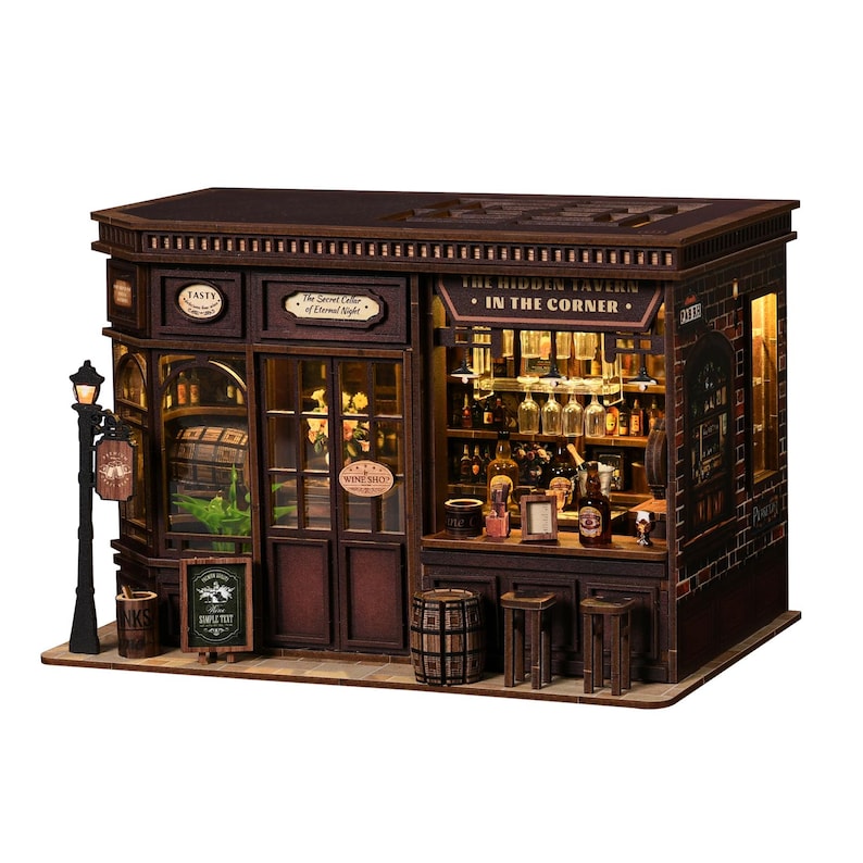 May include: A detailed miniature wooden tavern model. The sign above the entrance reads "The Hidden Tavern - In The Corner." The model includes a street lamp, barrels, and small stools. Interior lighting is visible through the windows, showcasing bottles and glasses.