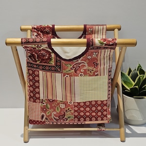 Peut inclure: Un panier à linge pliable en bois avec un sac en tissu patchwork. Le tissu présente des motifs floraux, cachemire et rayés dans des tons de rouge, rose et vert. Le cadre en bois est brun clair.