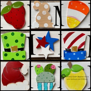 May include: Nine wooden signs with various painted designs. The signs feature a strawberry, bunny, candy corn, leprechaun hat, stars, a top hat, Santa hat, cactus, and an apple. The signs are all painted in bright colors and have a rustic, handmade look.