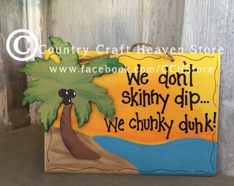 Peut inclure: Une pancarte en bois avec un palmier, une plage et un coucher de soleil peints. La pancarte indique "We don't skinny dip... We chunky dunk!"