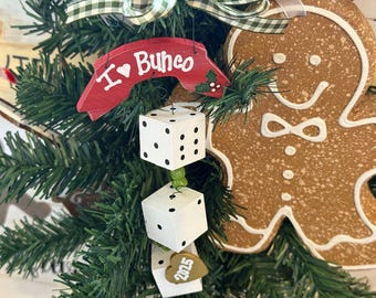 May include: A festive Christmas tree decorated with ornaments. The ornaments include a red sign that says "I ❤️ Bunco", dice, and a gingerbread man. The dice are white with black dots. A gold heart-shaped tag reads "2025".